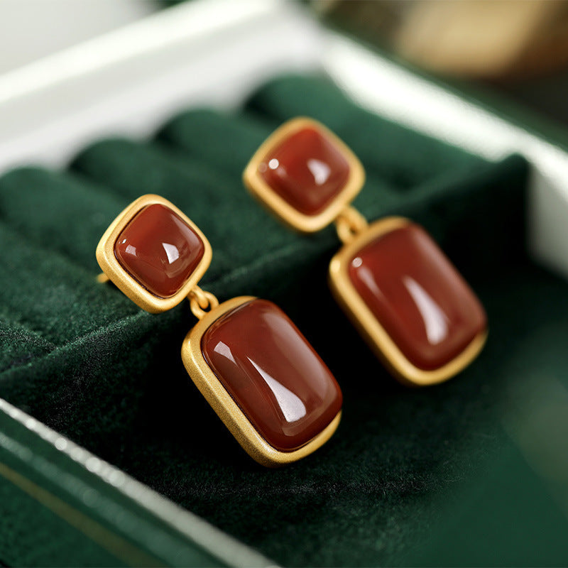 Pair of gold earrings with red stones on a green cushion