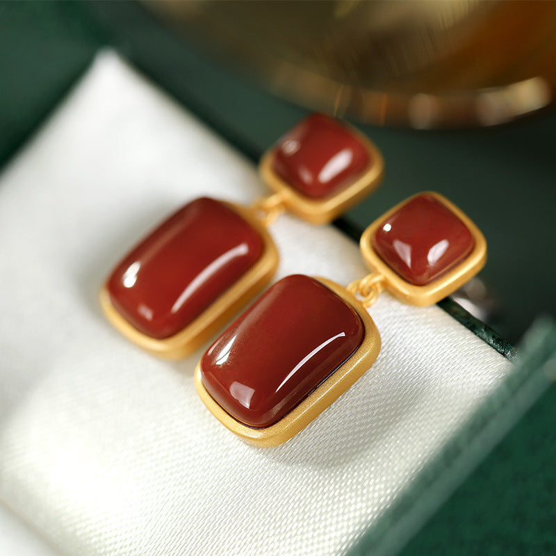 Pair of earrings with red stones and gold frames on a white surface.