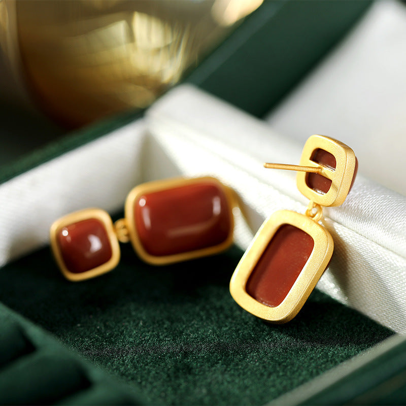 Gold earrings with red stones on a green and white fabric background