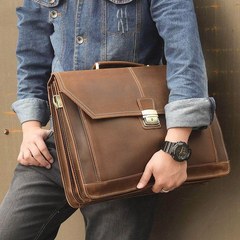 Person holding a brown leather briefcase with a denim jacket and gray pants.