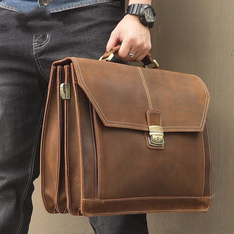 Brown leather briefcase held by a person wearing jeans and a watch.