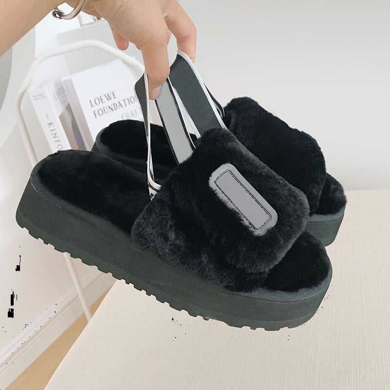 Black fuzzy slippers with a platform sole held by a hand on a light background