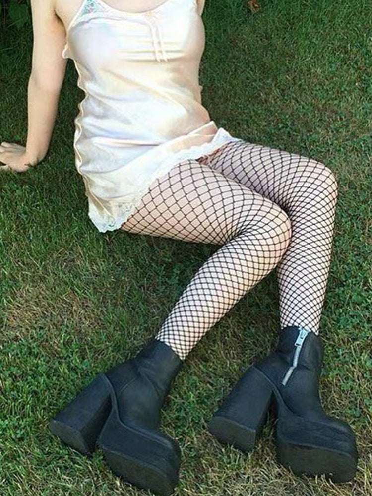 Person wearing fishnet stockings and black platform boots sitting on grass.