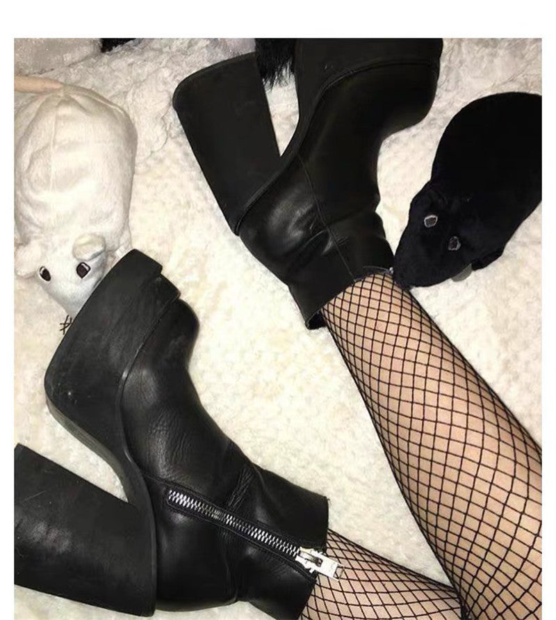 Black leather boots with zippers worn with fishnet stockings on a textured surface.