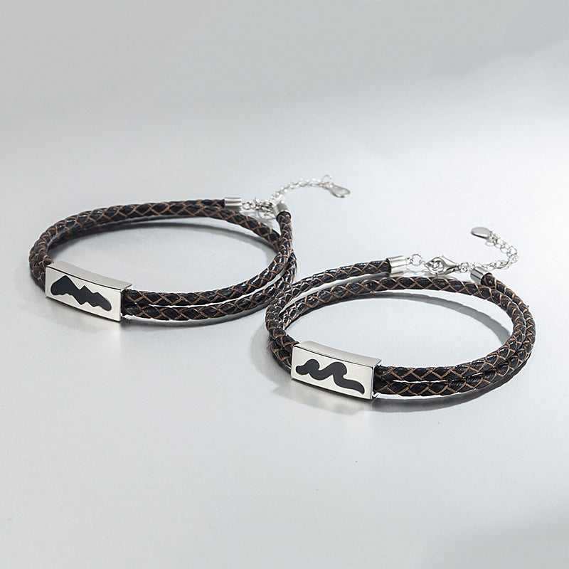Two braided leather bracelets with metal tags on a light gray background