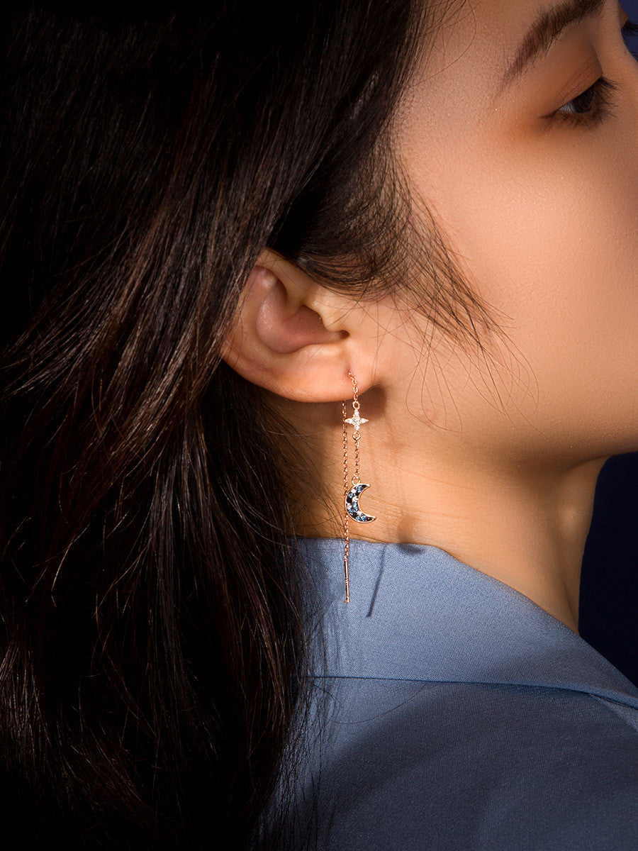 Close-up of a person wearing a delicate earring with a blue shirt against a dark background