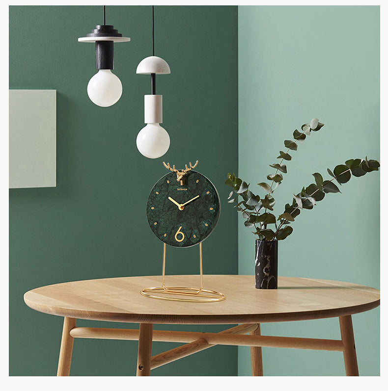 Decorative clock on a wooden table with modern pendant lights and a plant against a green wall.