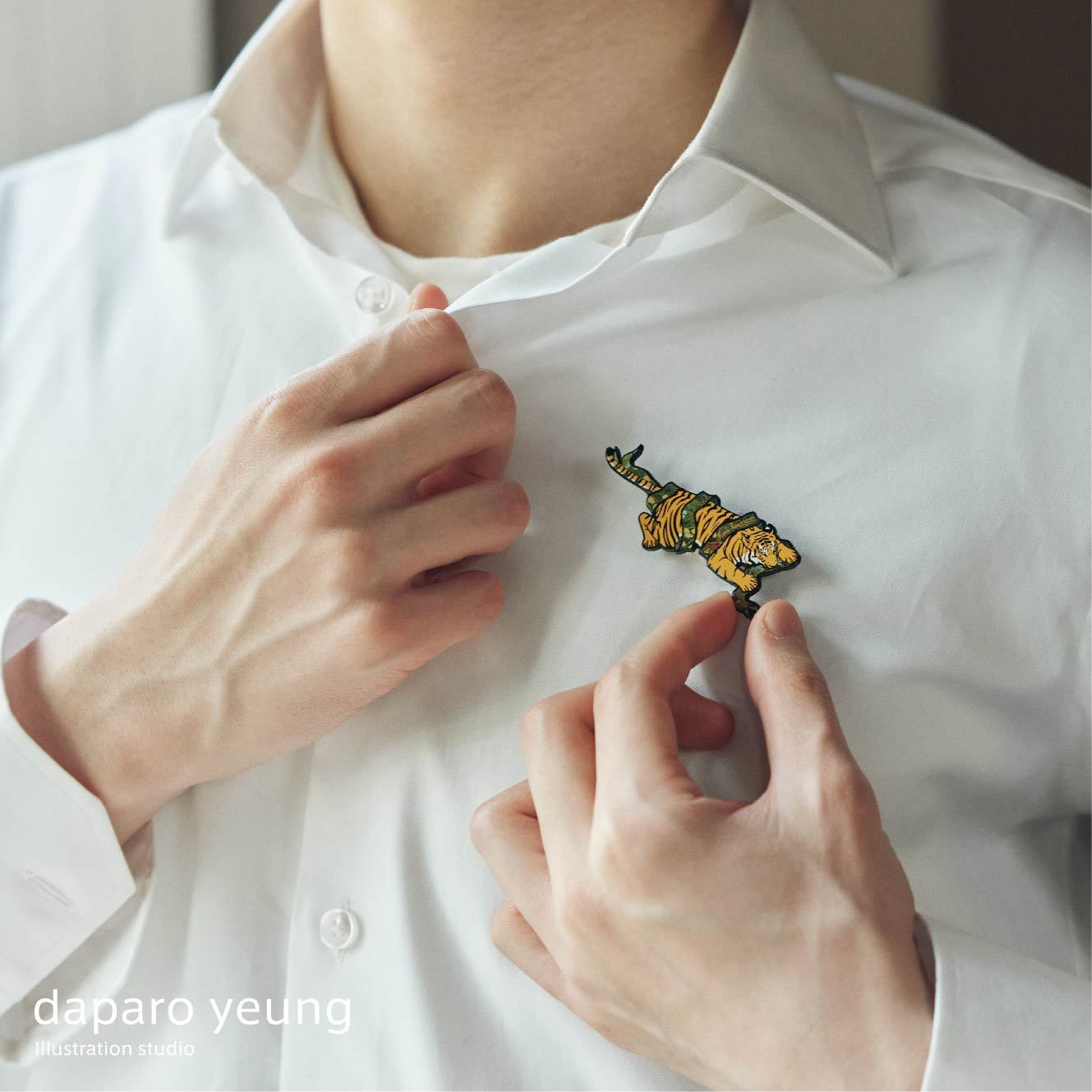 Person wearing a white shirt with a tiger brooch, with 'daparo yeung illustration studio' branding.