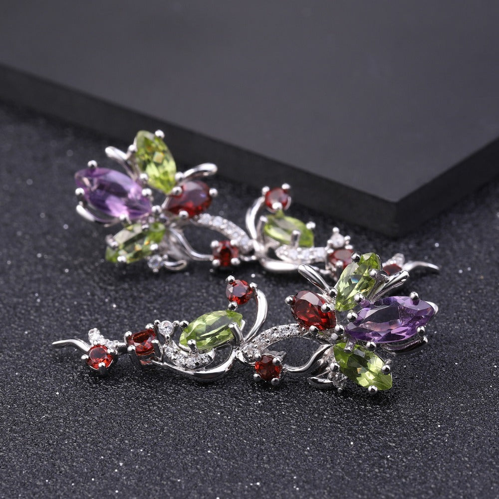 Pair of butterfly-shaped earrings with multicolored gemstones on a dark surface