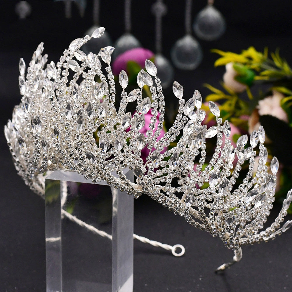 Silver tiara with intricate design on a stand against a dark background