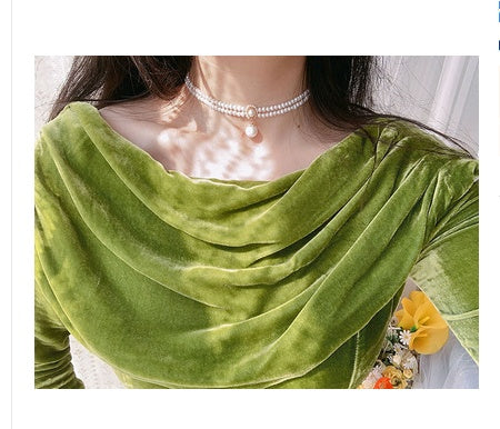 Green velvet garment with a pearl necklace and yellow flowers in the background