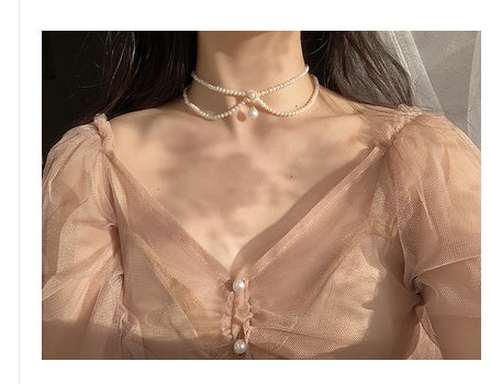Mannequin wearing a sheer beige dress with pearl details and a matching pearl necklace.