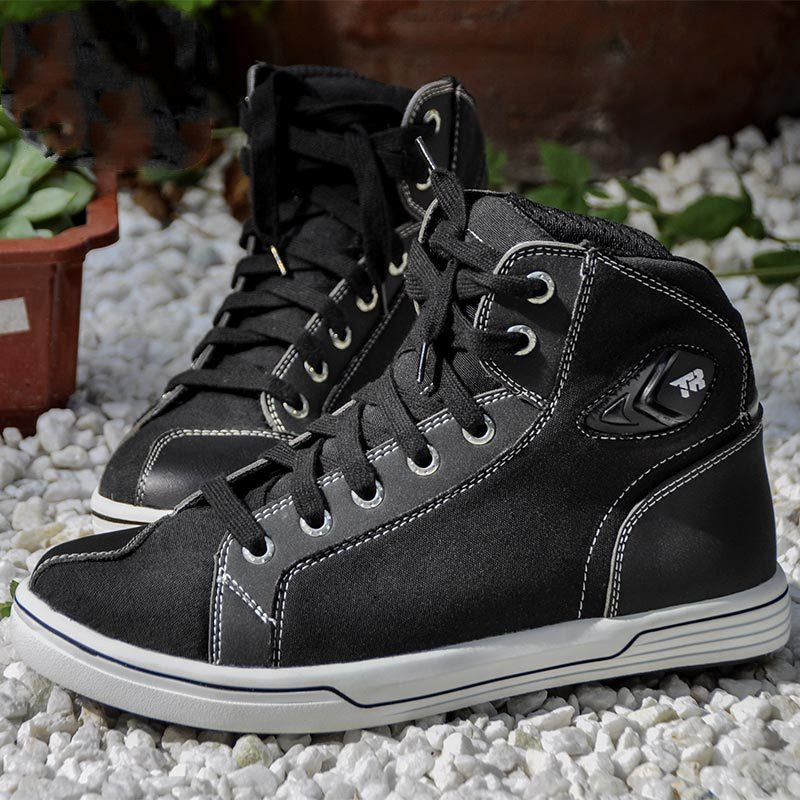 Black high-top sneakers on a gravel surface with plants in the background