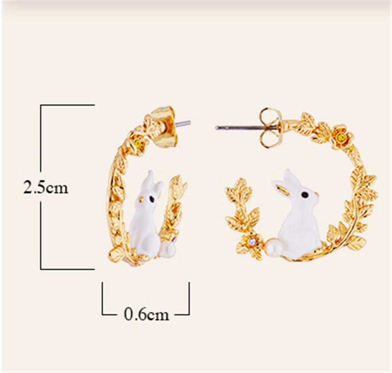Gold hoop earrings with white rabbit designs and measurements on a light pink background
