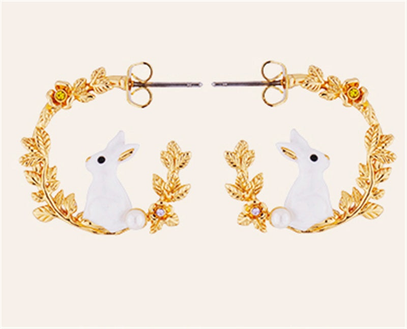 Pair of earrings with white rabbit design and gold leaf accents on a light pink background