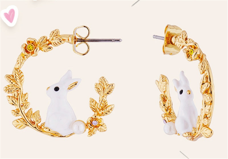 Gold hoop earrings with white rabbit designs on a light pink background