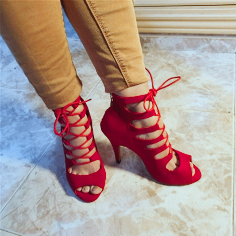 Red strappy high-heeled shoes worn with beige pants on a light marble floor.