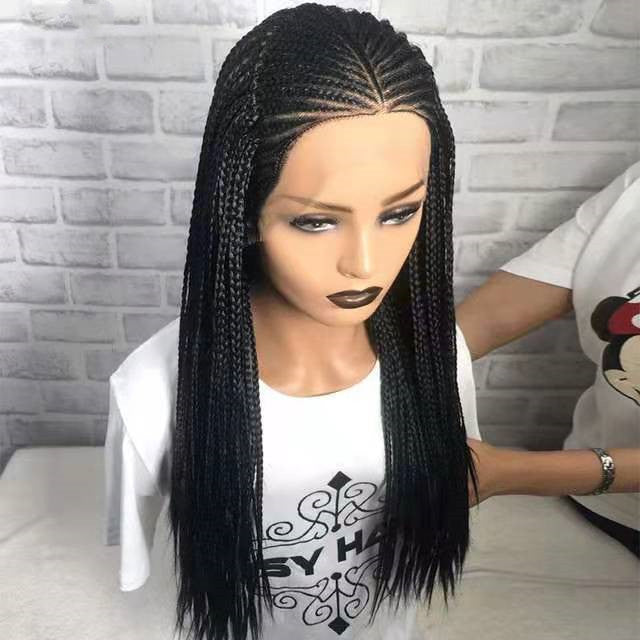 Person wearing a black braided wig with a white brick wall background