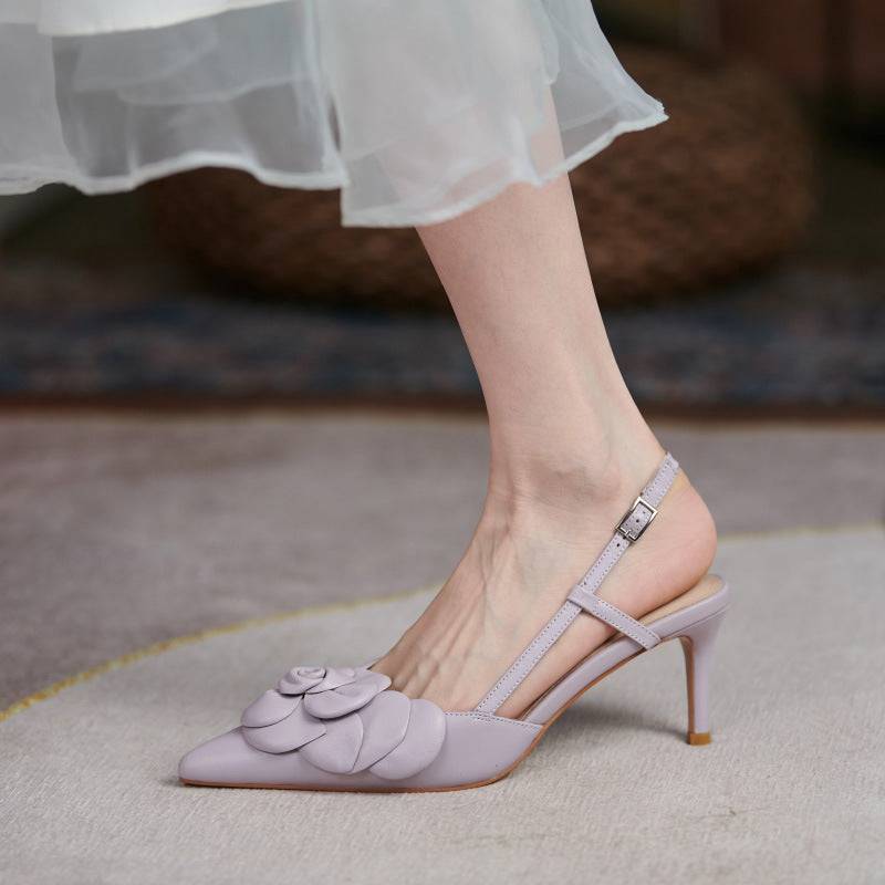 Light purple high-heeled shoes with floral design worn by a person in a white dress.
