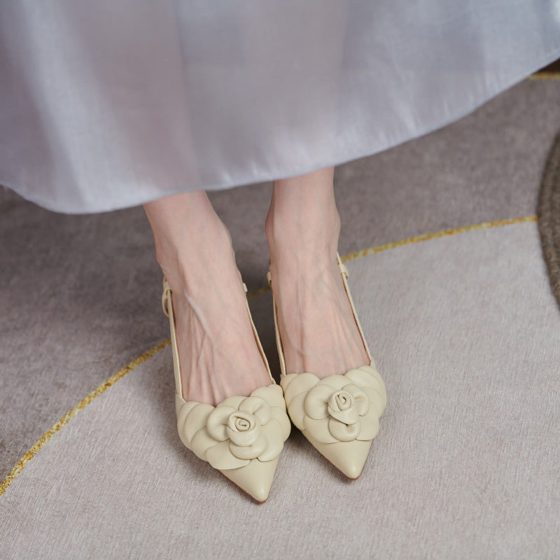 Beige high-heeled shoes with floral details worn by a person in a light-colored dress on a textured floor.