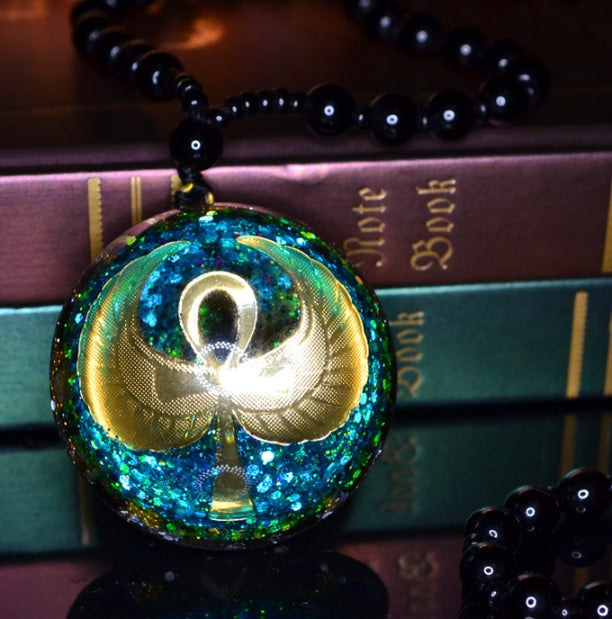 Necklace with a glowing pendant featuring an ankh symbol on a stack of books.