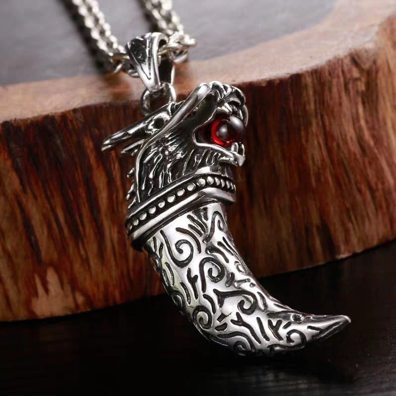 Silver dragon claw pendant with red gemstone on a wooden block