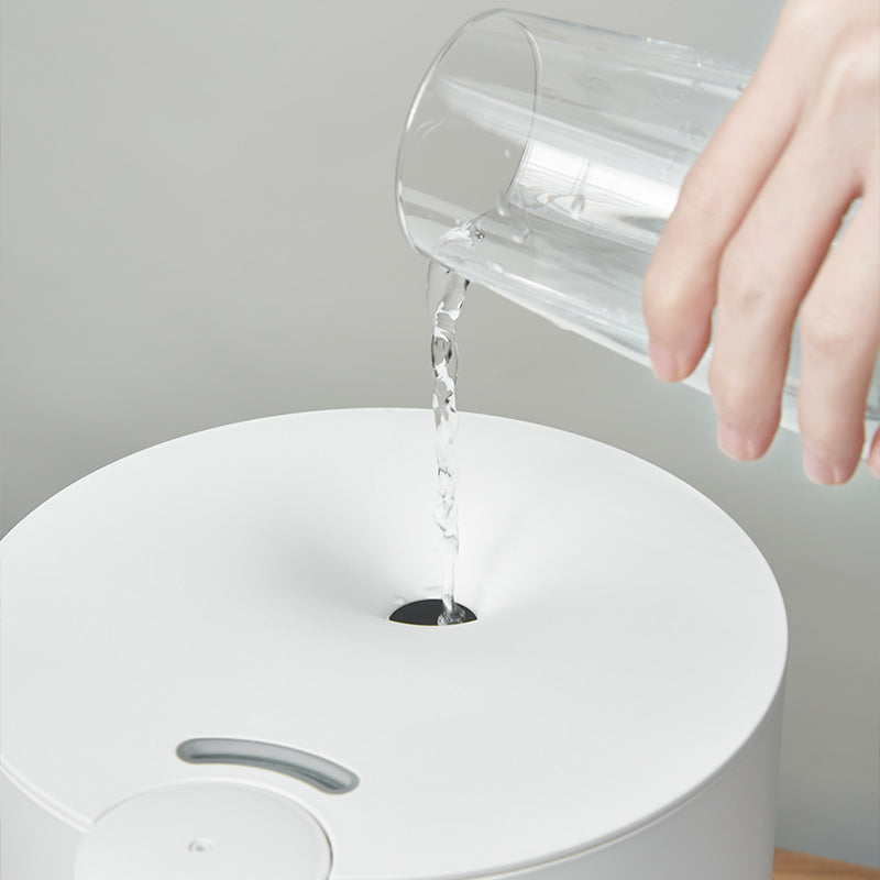 Person pouring water from a clear glass into a white humidifier.