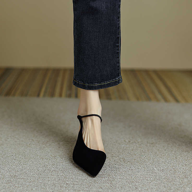 Black high-heeled shoes worn with dark jeans on a neutral background