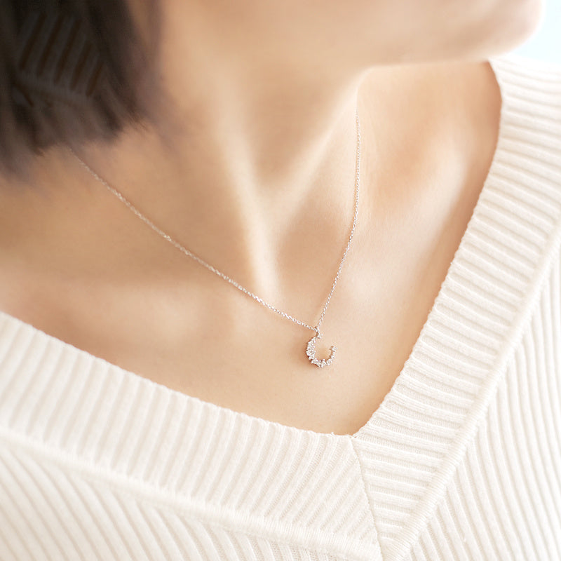 Silver necklace with a small pendant on a person wearing a white sweater.