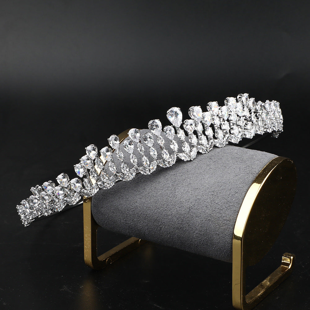 Silver tiara on a gray cushion with gold stand against a black background