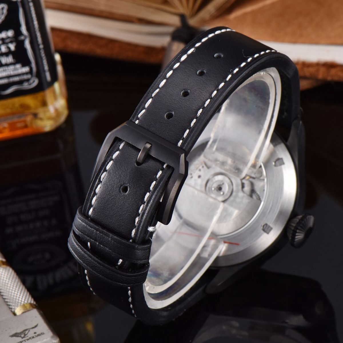 Watch with black leather strap and visible mechanism, bottle of Jack Daniel's in the background