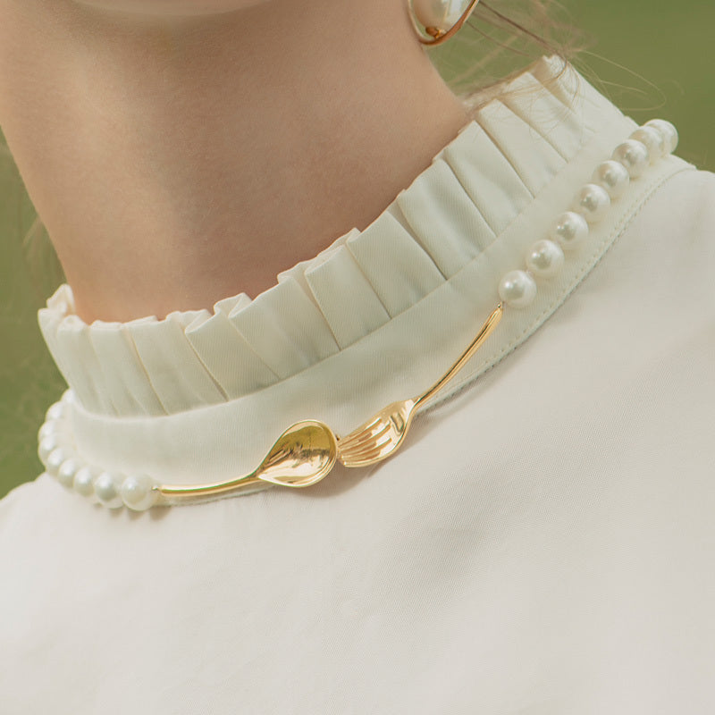 Gold necklace with leaf design and pearl accents worn by a person in a white outfit.