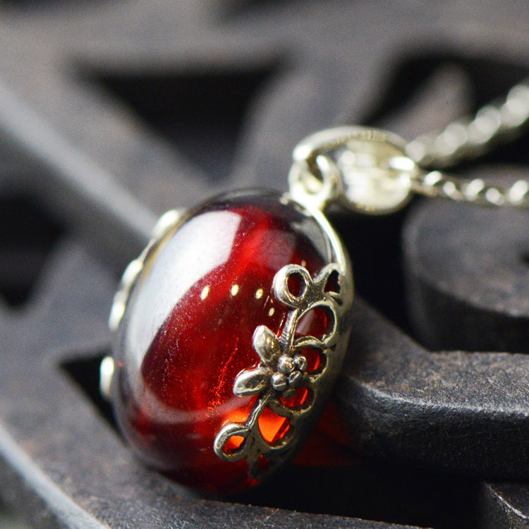 Red glass pendant with silver floral design on a dark textured background