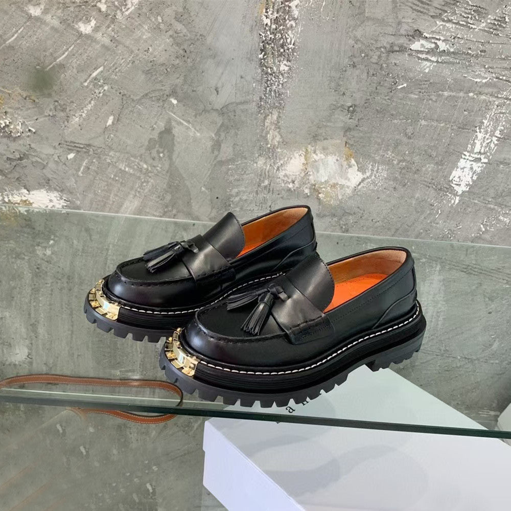 Black loafers with tassels on a glass surface against a textured gray background