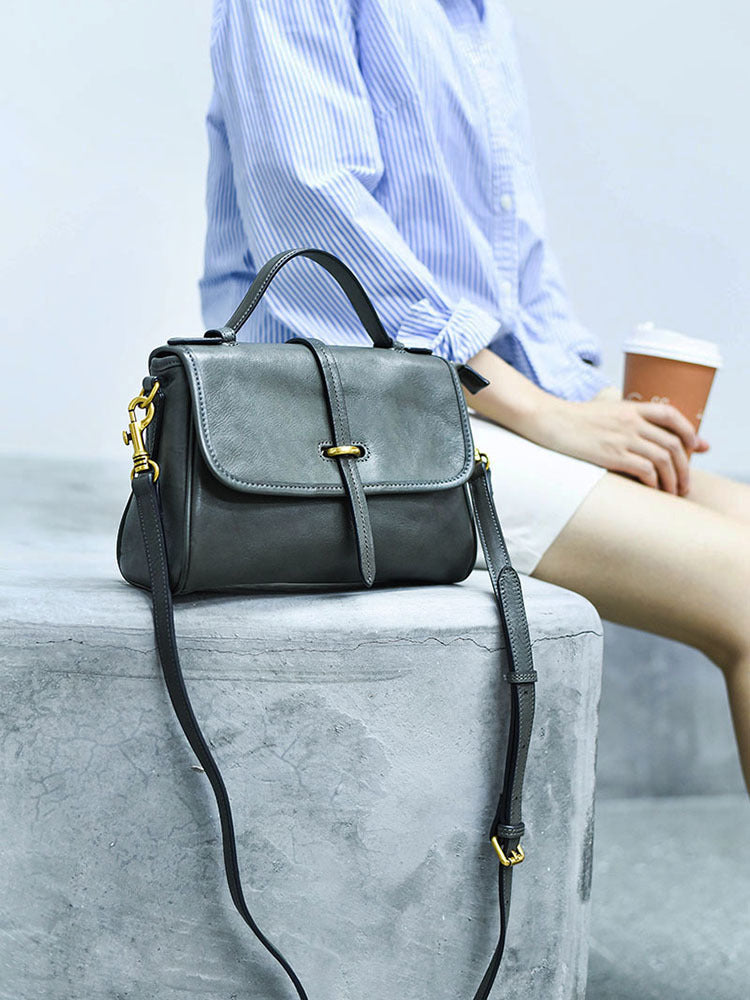 Gray handbag with gold accents on a light gray surface, person holding a coffee cup in the background.