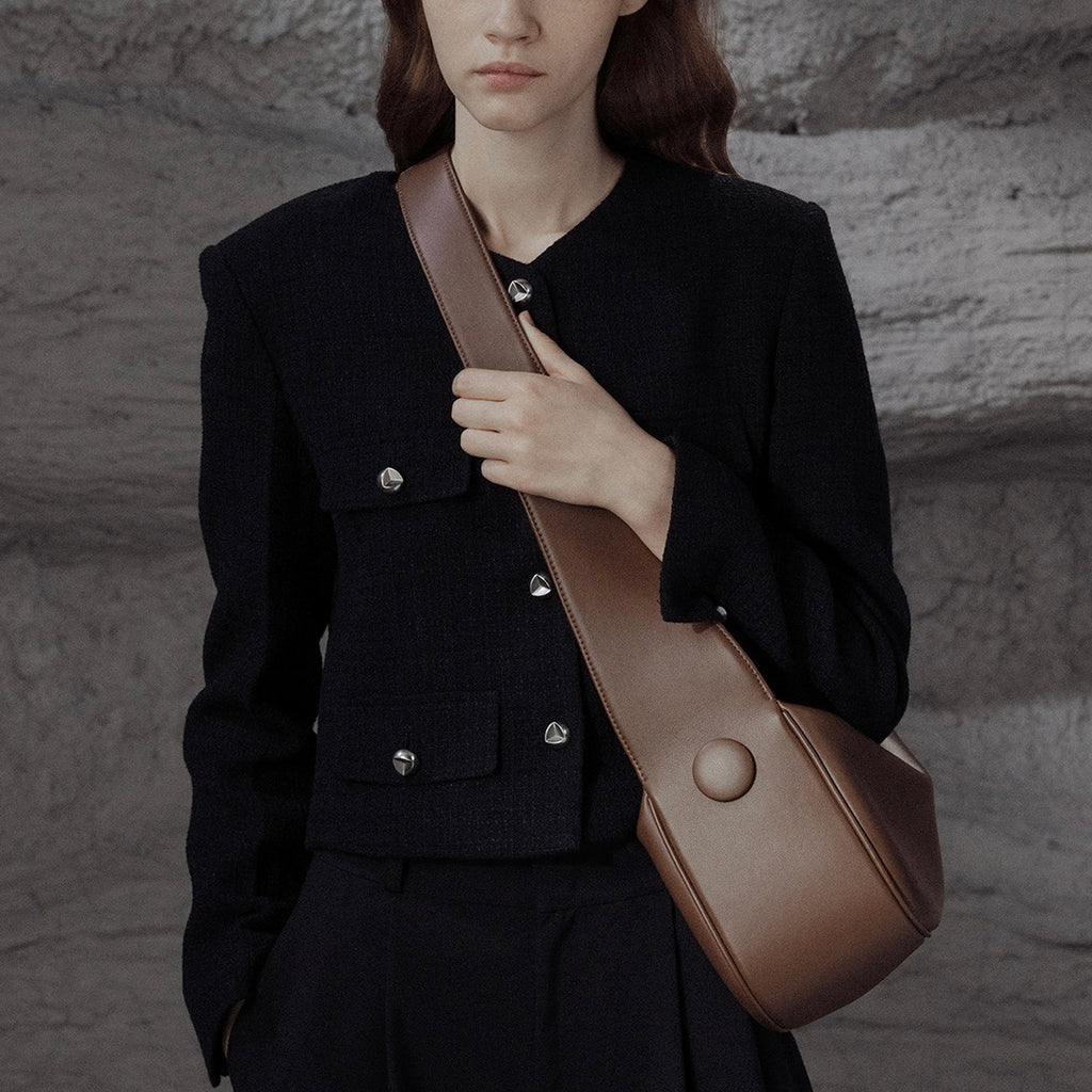Person wearing a black coat holding a brown leather bag against a textured wall.