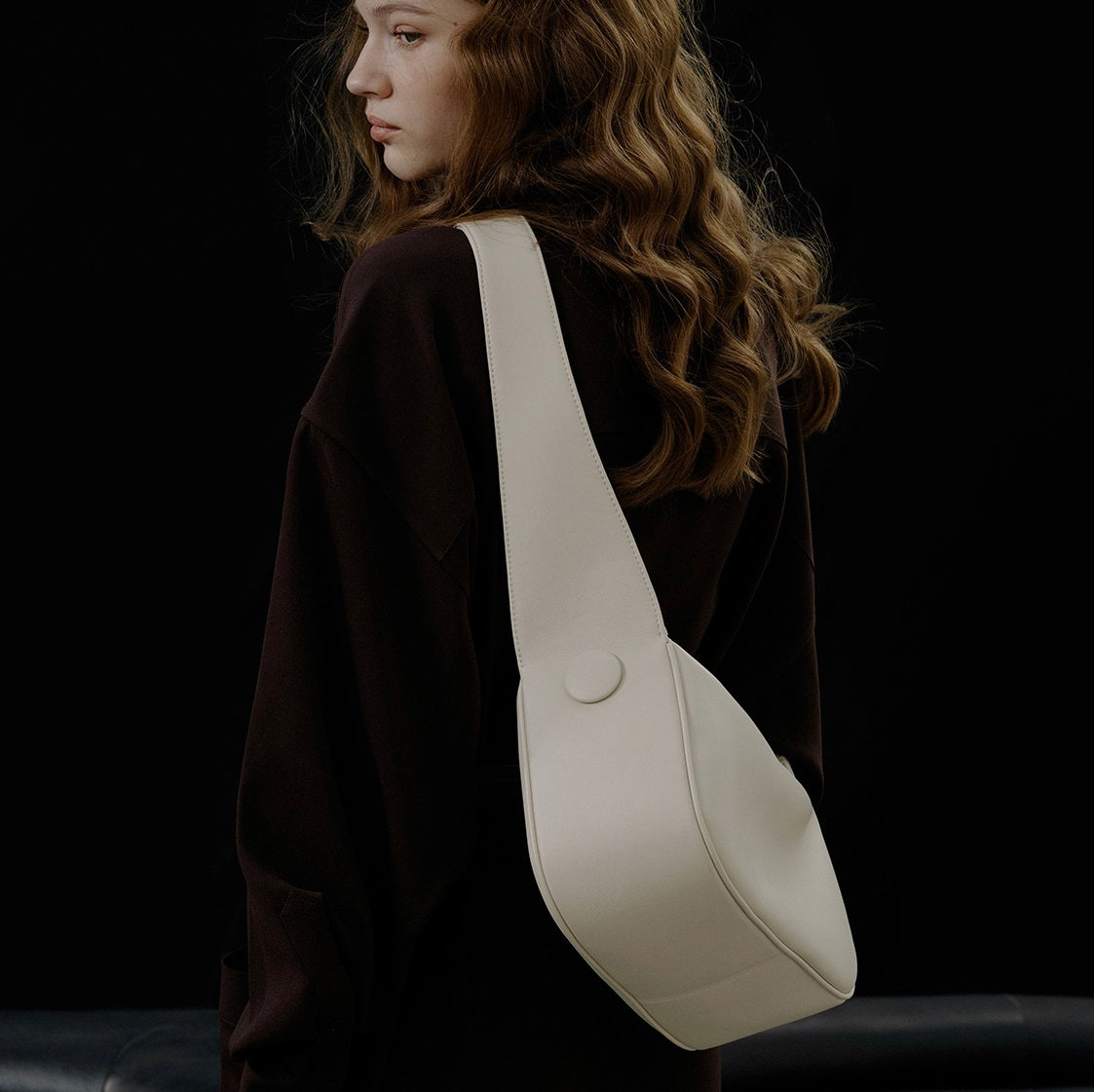 Woman carrying a white shoulder bag against a black background