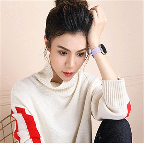 Woman wearing a white sweater with red accents and a smartwatch on a beige background