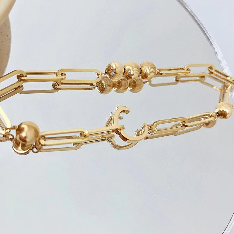 Gold bracelet with chain and bead design on a light gray background