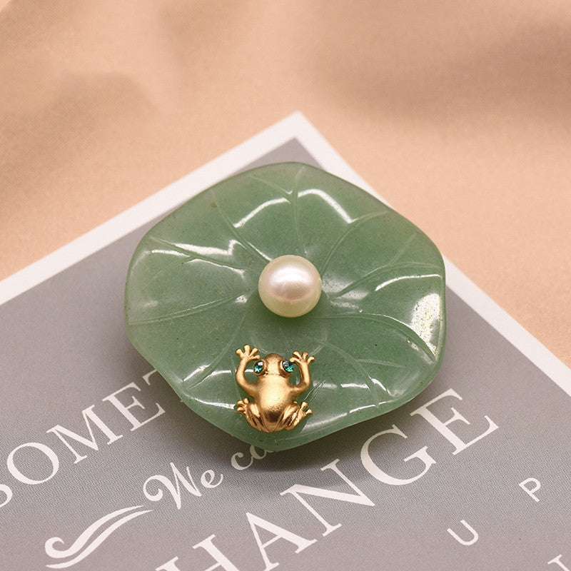 Green jade pendant with a pearl and gold frog on a beige surface