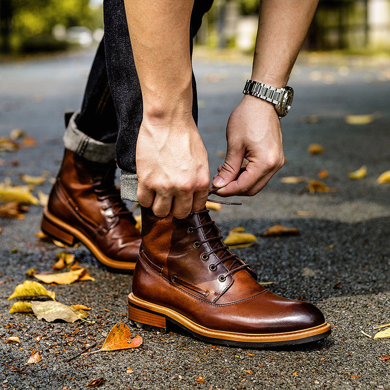Person tying a brown leather boot on a street with leaves