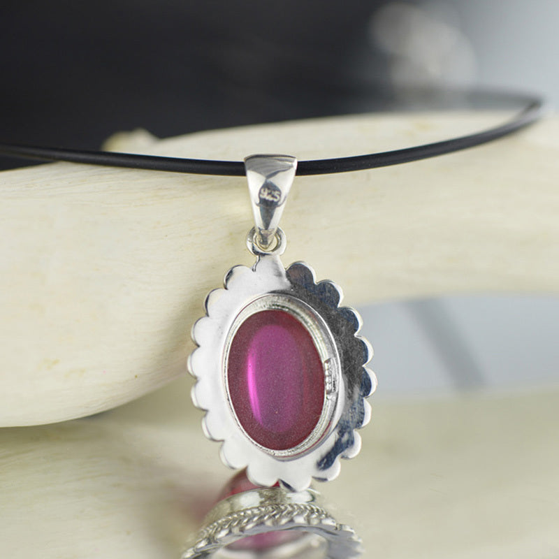 Silver pendant with a pink stone on a black cord, displayed on a neutral background.