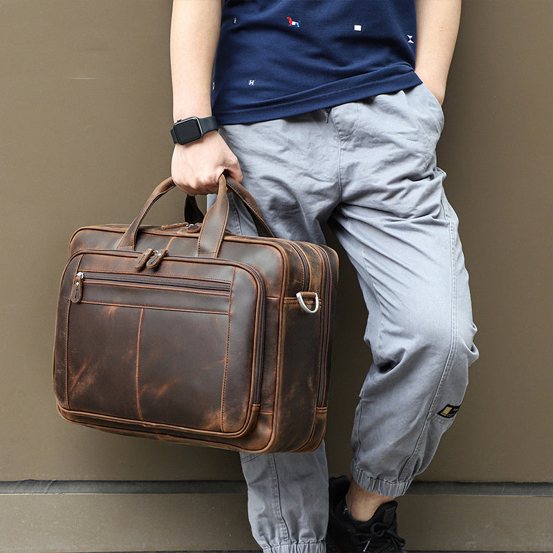 Person holding a brown leather briefcase against a plain background
