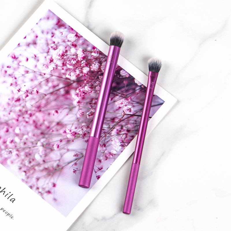 Two purple makeup brushes on a white surface with a floral background