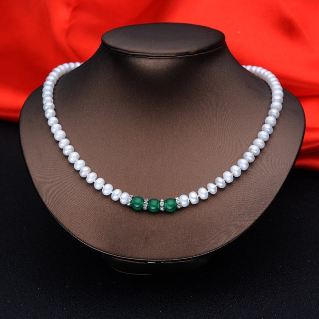 Pearl necklace with green beads on a mannequin against a red fabric background