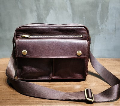Brown leather bag with gold zippers and studs on a wooden surface with a gray background