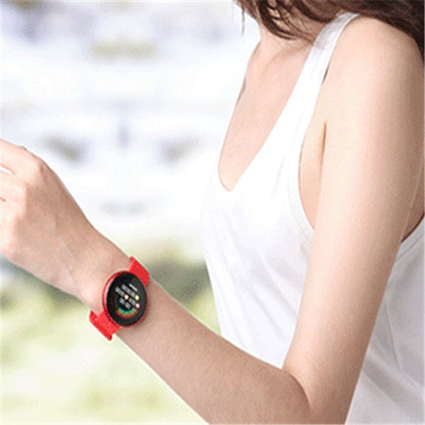 Person wearing a red smartwatch with a blurred natural background