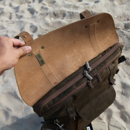 Brown leather bag held by a hand on a sandy background