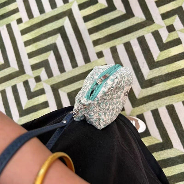 Small floral-patterned pouch with a turquoise zipper on a person's lap against a geometric-patterned background.