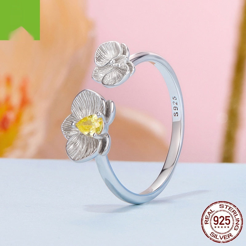 Silver ring with floral designs and a yellow gemstone on a light background
